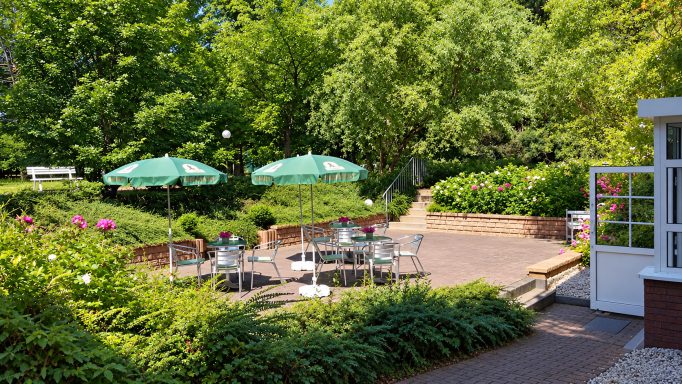 Gartenterrasse der Unikum Pension in Wolfen mit Tischen, Stühlen und grünen Sonnenschirmen im Schatten der Bäume.