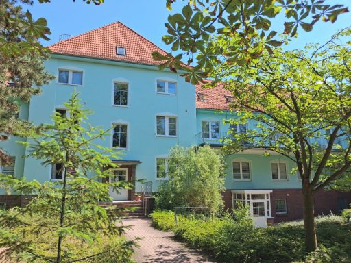 Außenansicht der Unikum Pension in Wolfen mit blauem Gebäude, rotem Ziegeldach und grüner Gartenanlage.