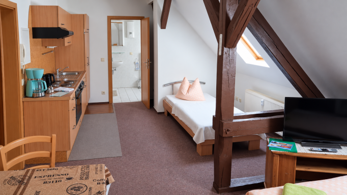 Innenansicht eines Appartements der Unikum Pension mit Bett, Dachschräge und sichtbaren Holzbalken.